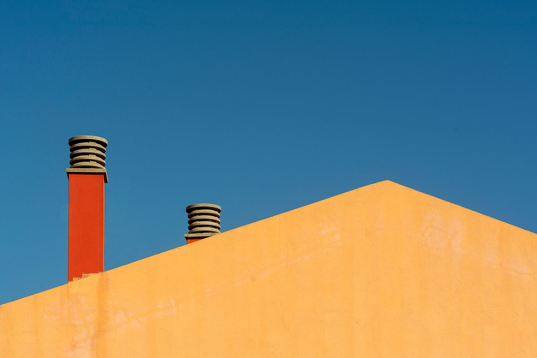 Minimalist photo of a building facade with chimneys against a clear blue sky.