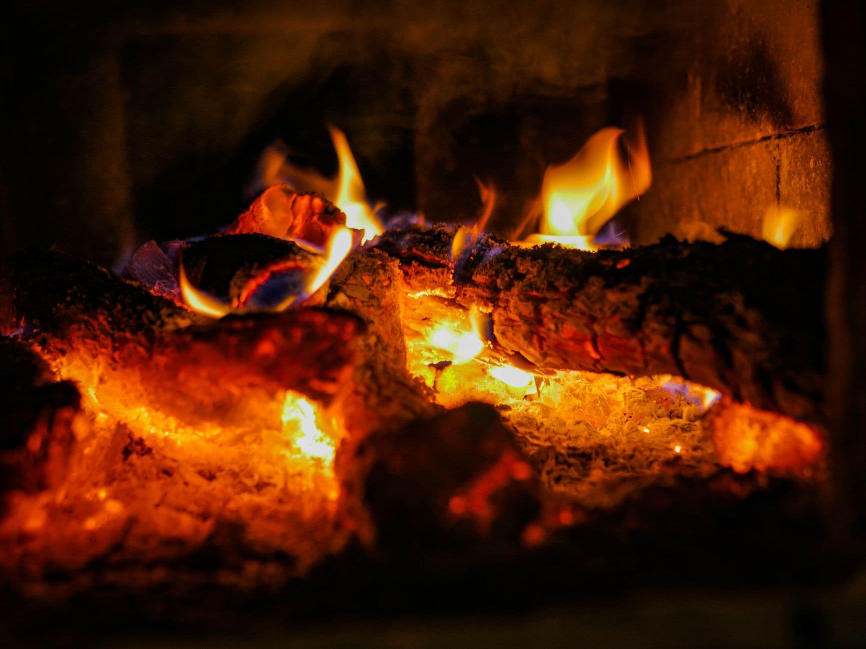 A warm close-up of burning logs producing vibrant flames in a cozy fireplace.